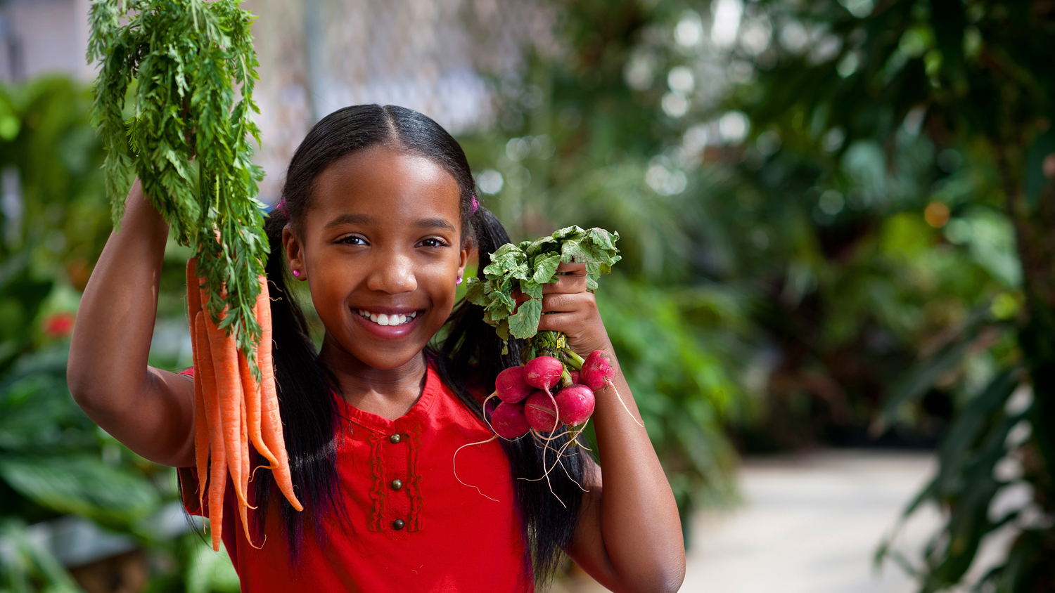 Girl holding carrots and radishes while standing in a garden.